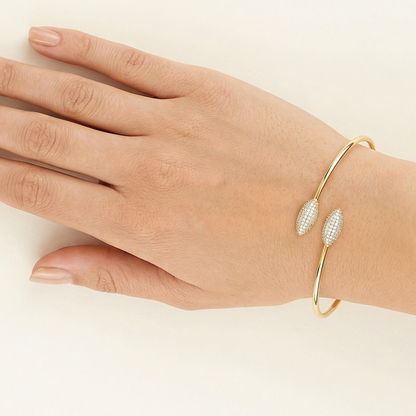 Gold bracelet with leaf-like designs on a hand against a beige background
