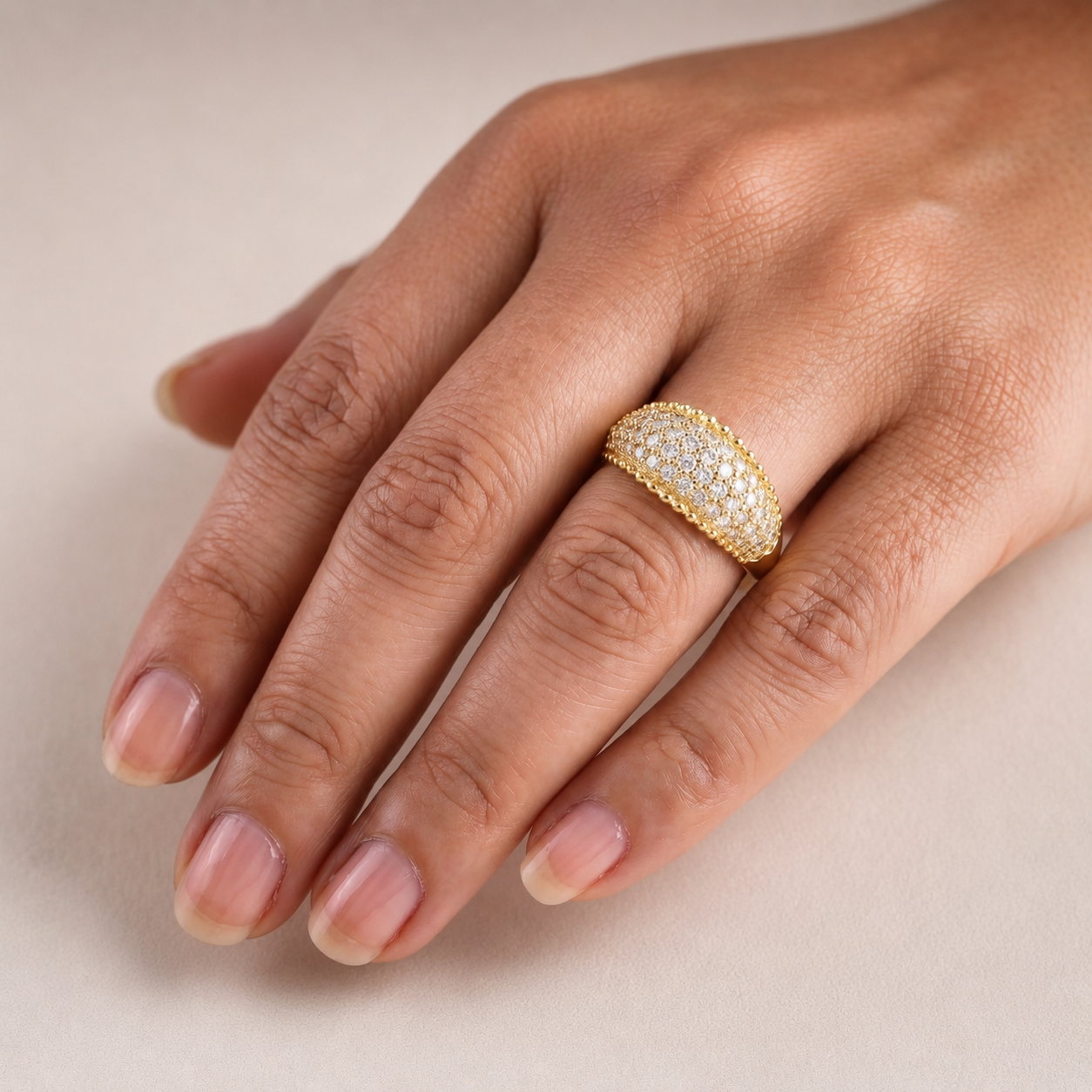 Gold ring with diamonds on a hand against a beige background