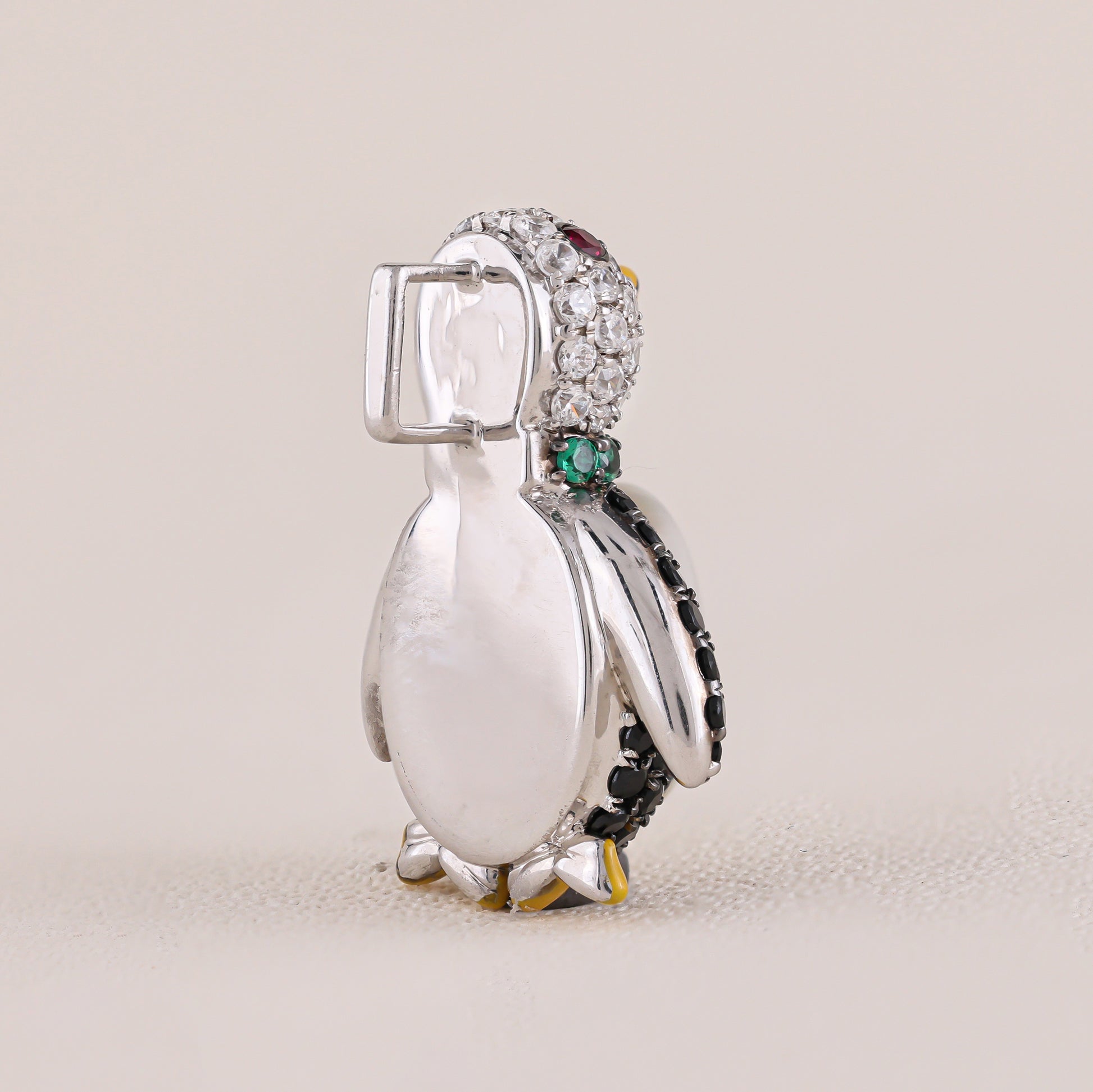 Penguin-shaped jewelry charm with gemstones on a beige background