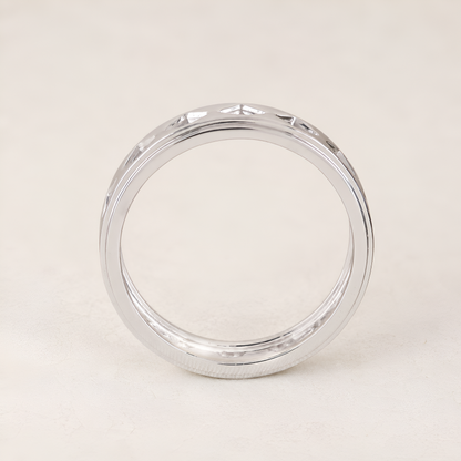 A polished silver band ring with a beveled edge and a subtle textured pattern on the outer surface, displayed on a light beige background.