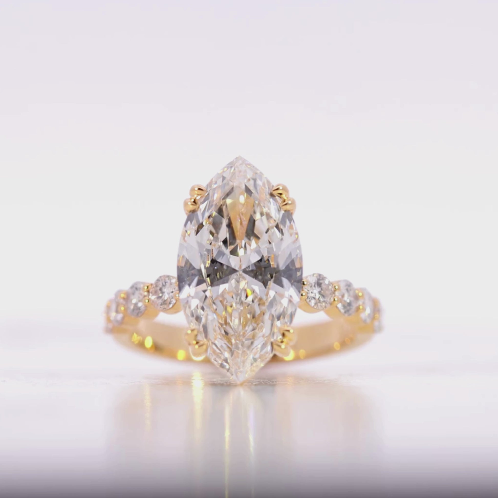 Gold ring with a large diamond and smaller diamonds on the band against a beige background Video