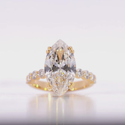 Gold ring with a large diamond and smaller diamonds on the band against a beige background Video