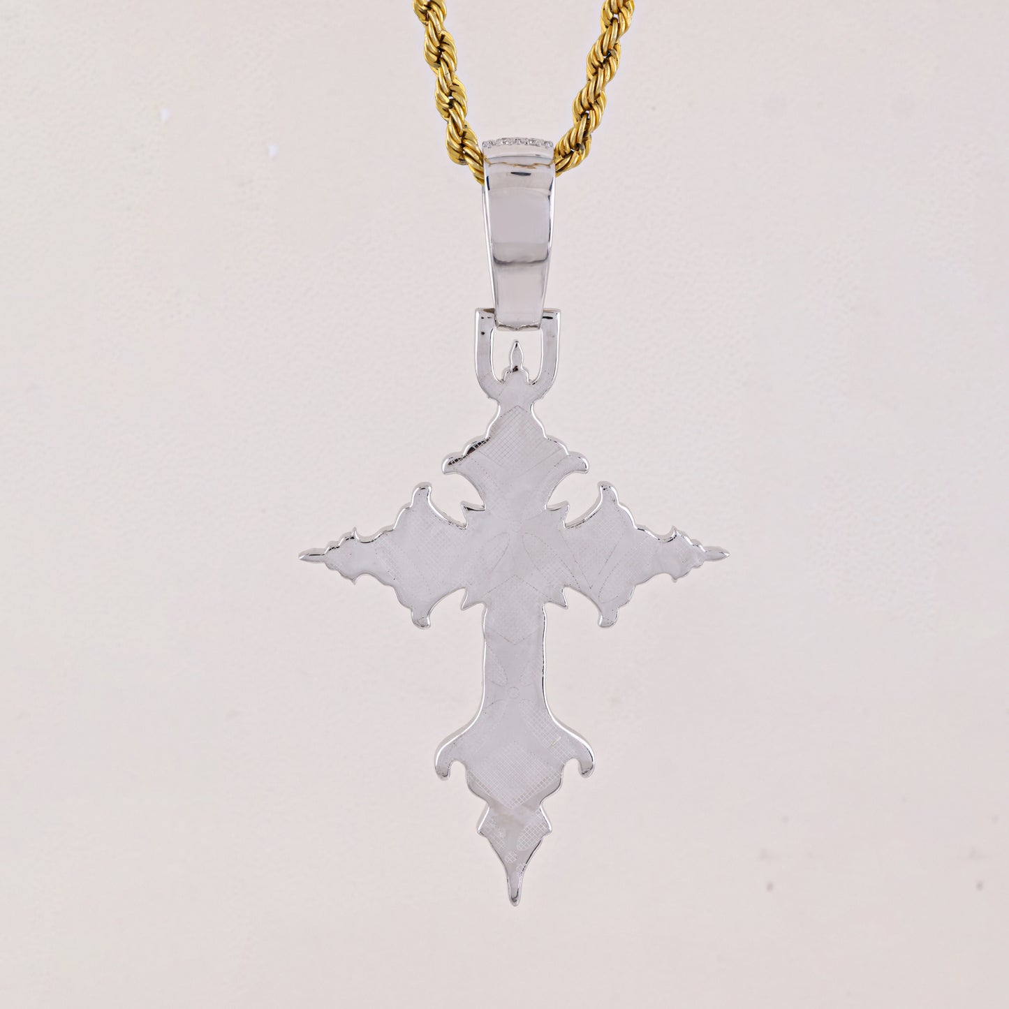 Silver cross pendant on a gold chain against a light gray background