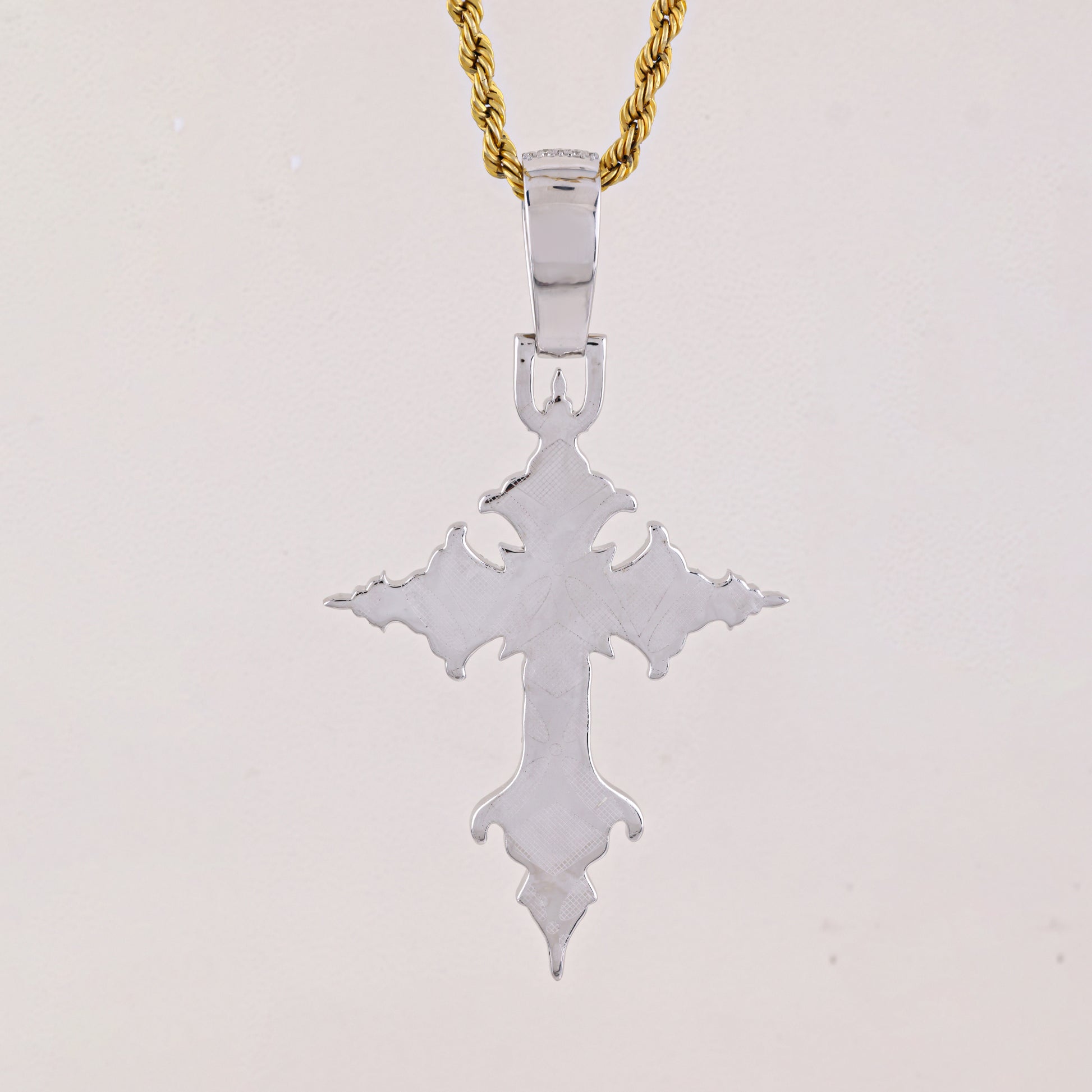 Silver cross pendant on a gold chain against a light gray background