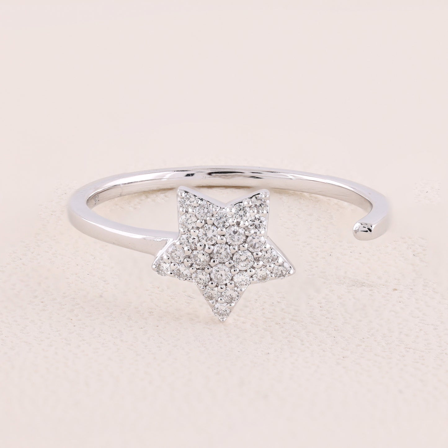 Silver ring with a star-shaped diamond design on a light pink background