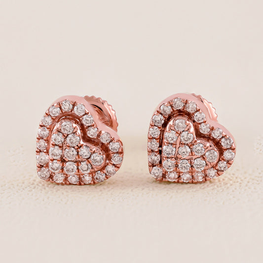 Heart-shaped earrings with rose gold and clear gemstones on a beige background