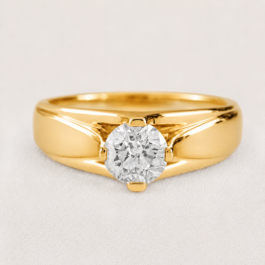A yellow gold solitaire ring featuring a round brilliant-cut diamond set in a four-prong setting, photographed on a light gray textured background.