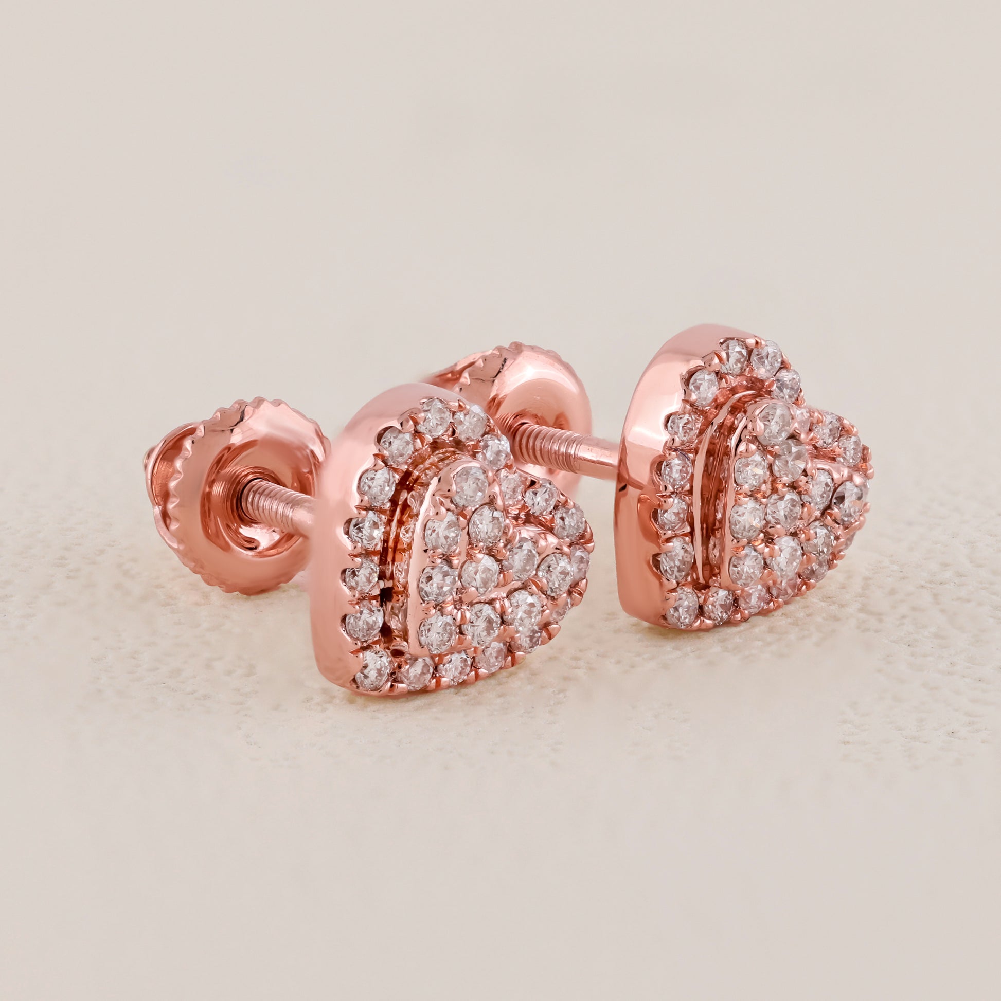 Rose gold heart-shaped earrings with clear gemstones on a beige background