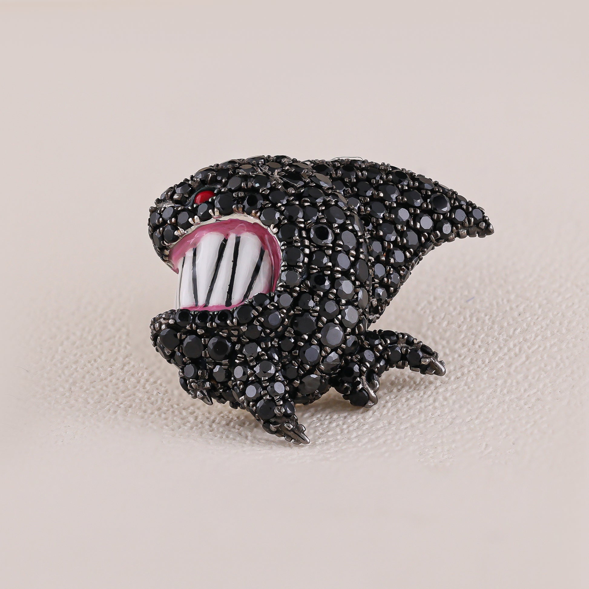 Black shark-shaped brooch with white teeth and red eye on a beige background