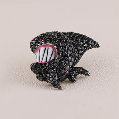 Black shark-shaped brooch with white teeth and red eye on a beige background