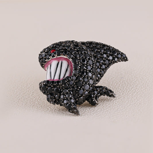 Black shark-shaped brooch with white teeth and red eye on a beige background
