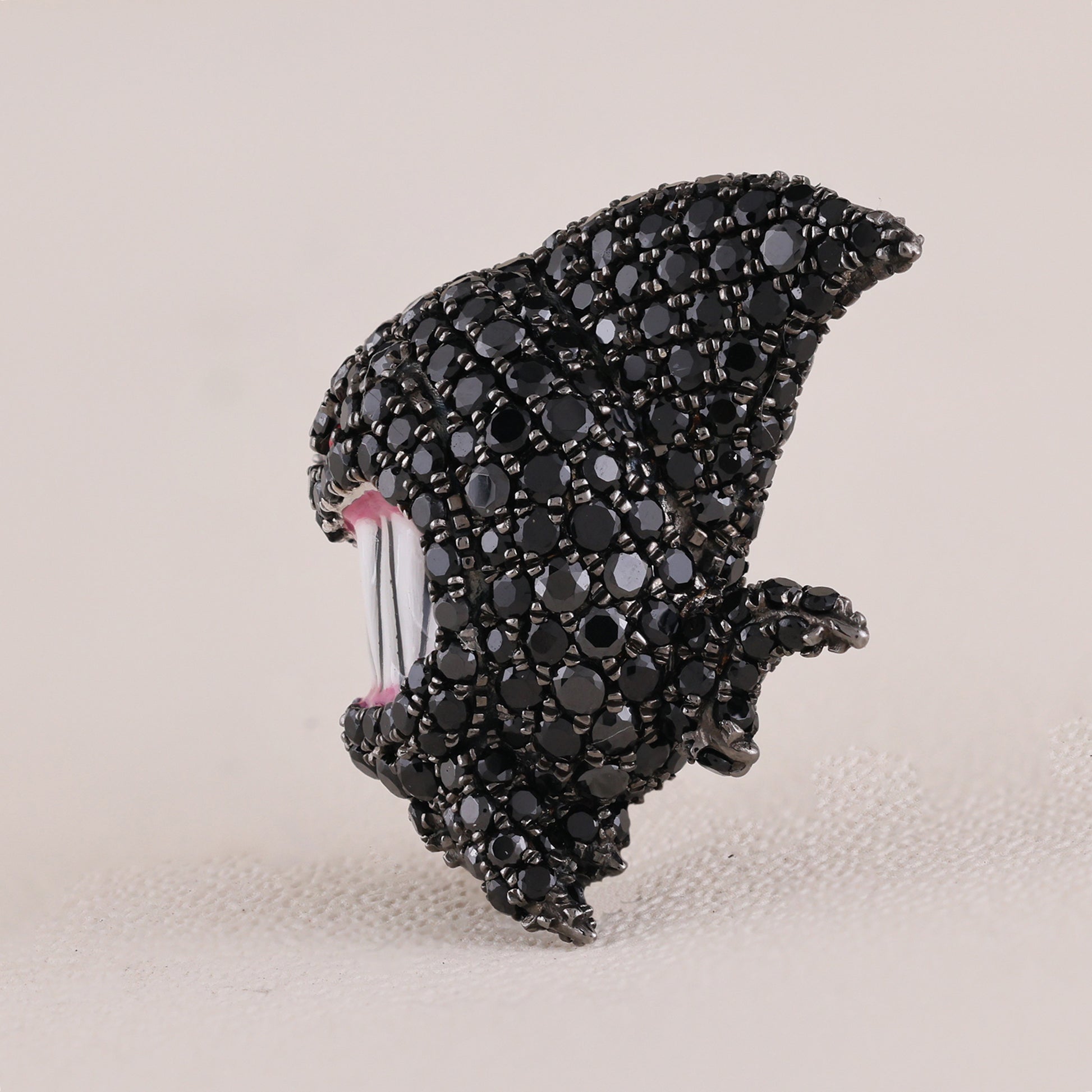 Black jeweled shark tooth brooch on a beige background