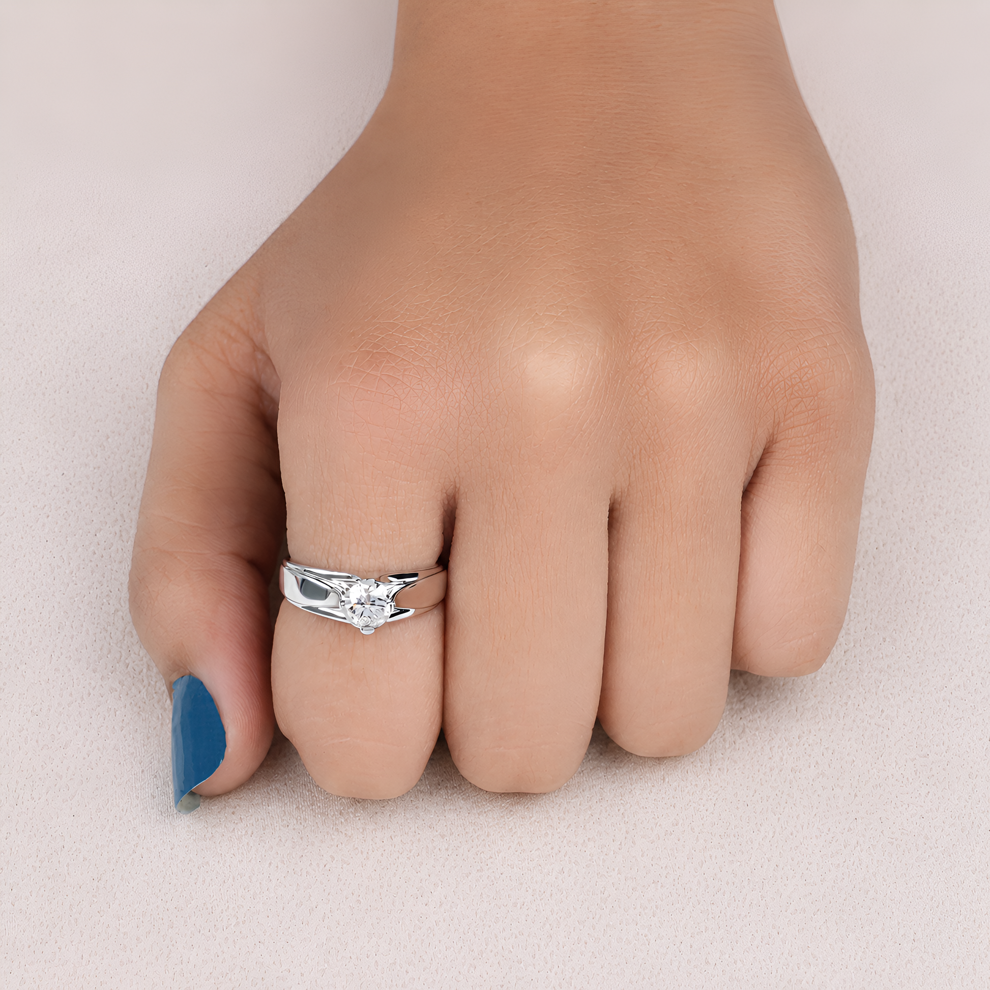 A silver ring with a clear heart-shaped gemstone worn on a person's ring finger, shown against a soft beige background.