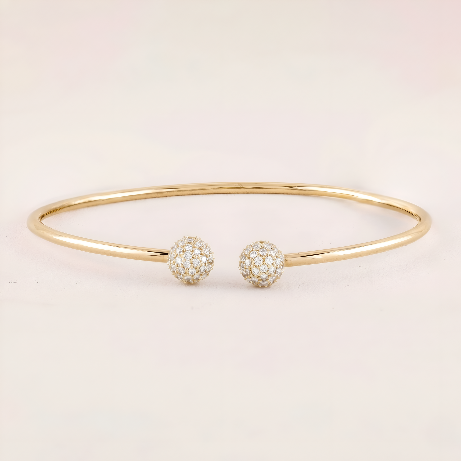 Gold bracelet with two spherical charms on a light beige background