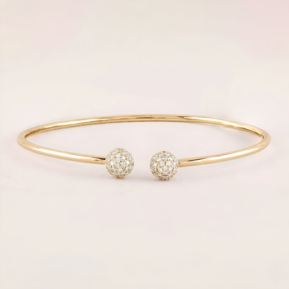 Gold bracelet with two spherical charms on a light beige background