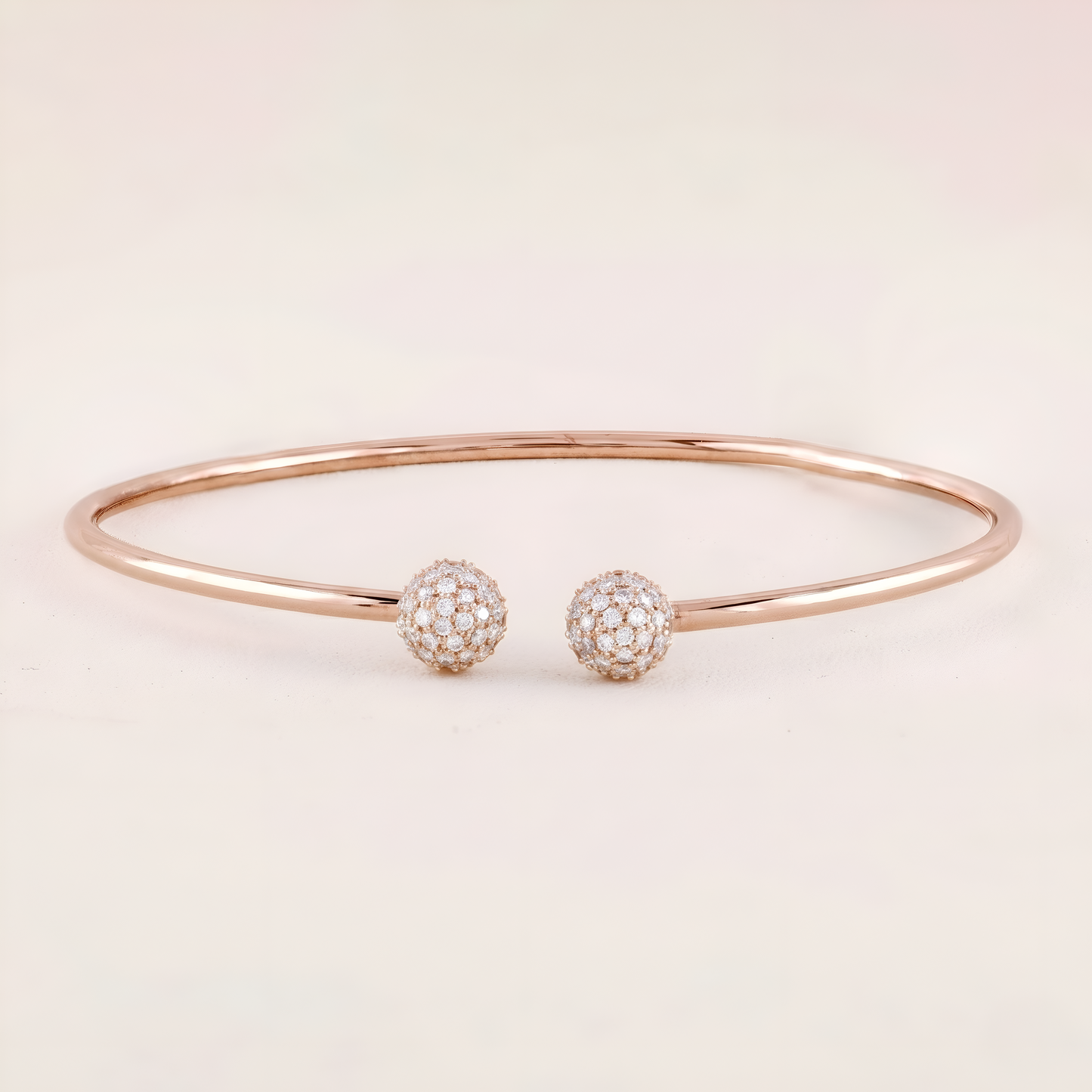Rose gold bracelet with two diamond-encrusted spherical charms on a light pink background