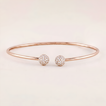 Rose gold bracelet with two diamond-encrusted spherical charms on a light pink background