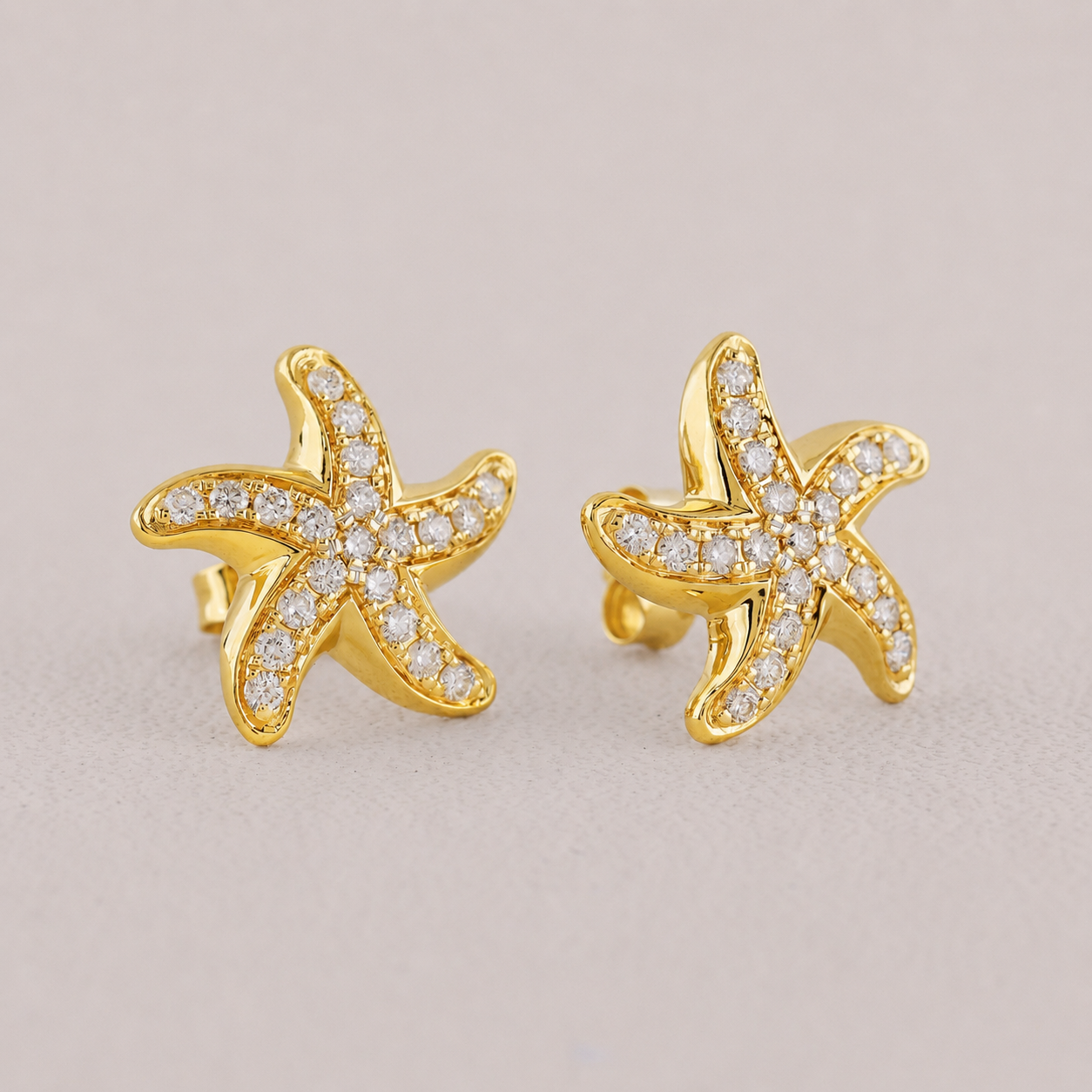 Gold starfish earrings with diamond accents on a beige background