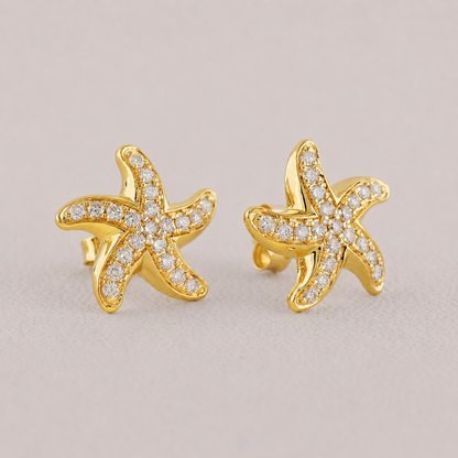 Gold starfish earrings with diamond accents on a beige background