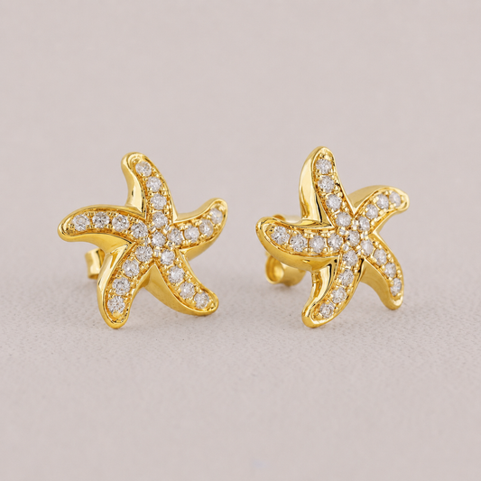 Gold starfish earrings with diamond accents on a beige background