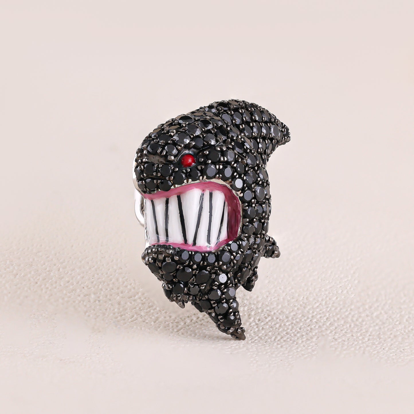 Jewelry item resembling a stylized face with black rhinestones on a beige background