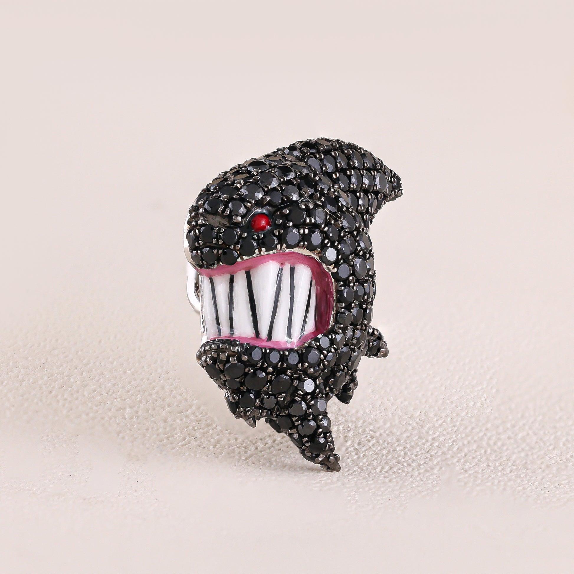 Jewelry item resembling a stylized face with black rhinestones on a beige background