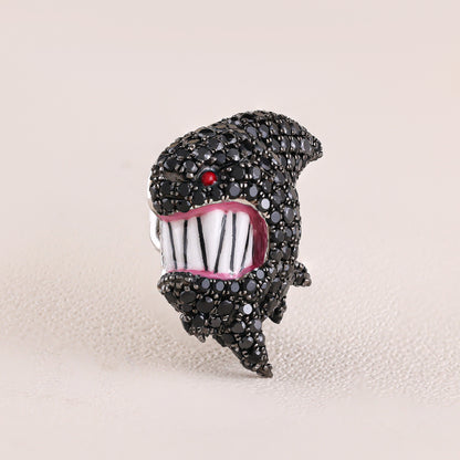 Jewelry item resembling a stylized face with black rhinestones on a beige background