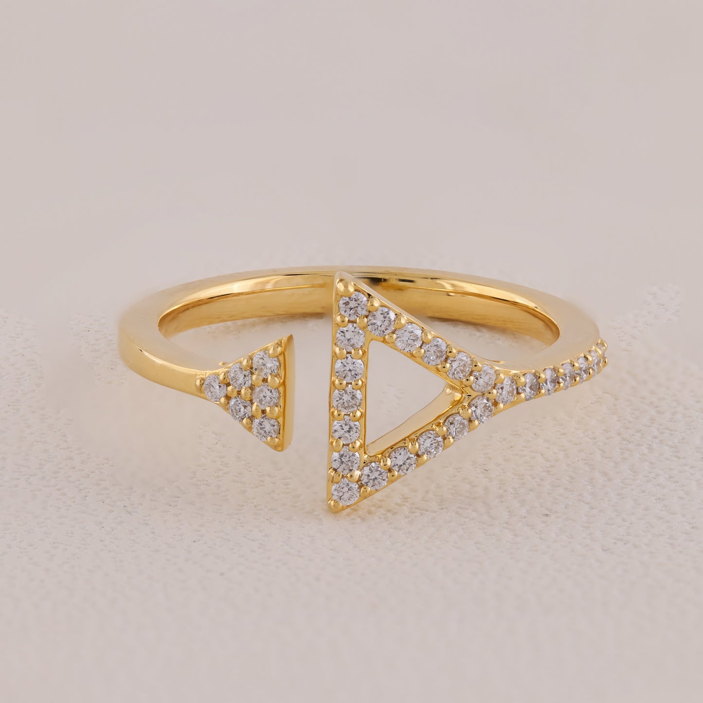 Gold ring with triangular design and embedded diamonds on a beige background