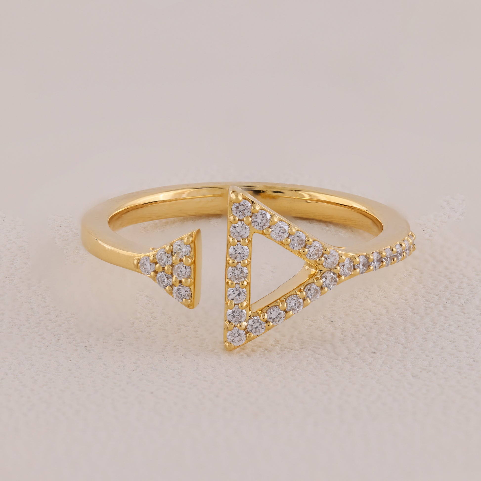 Gold ring with triangular design and embedded diamonds on a beige background
