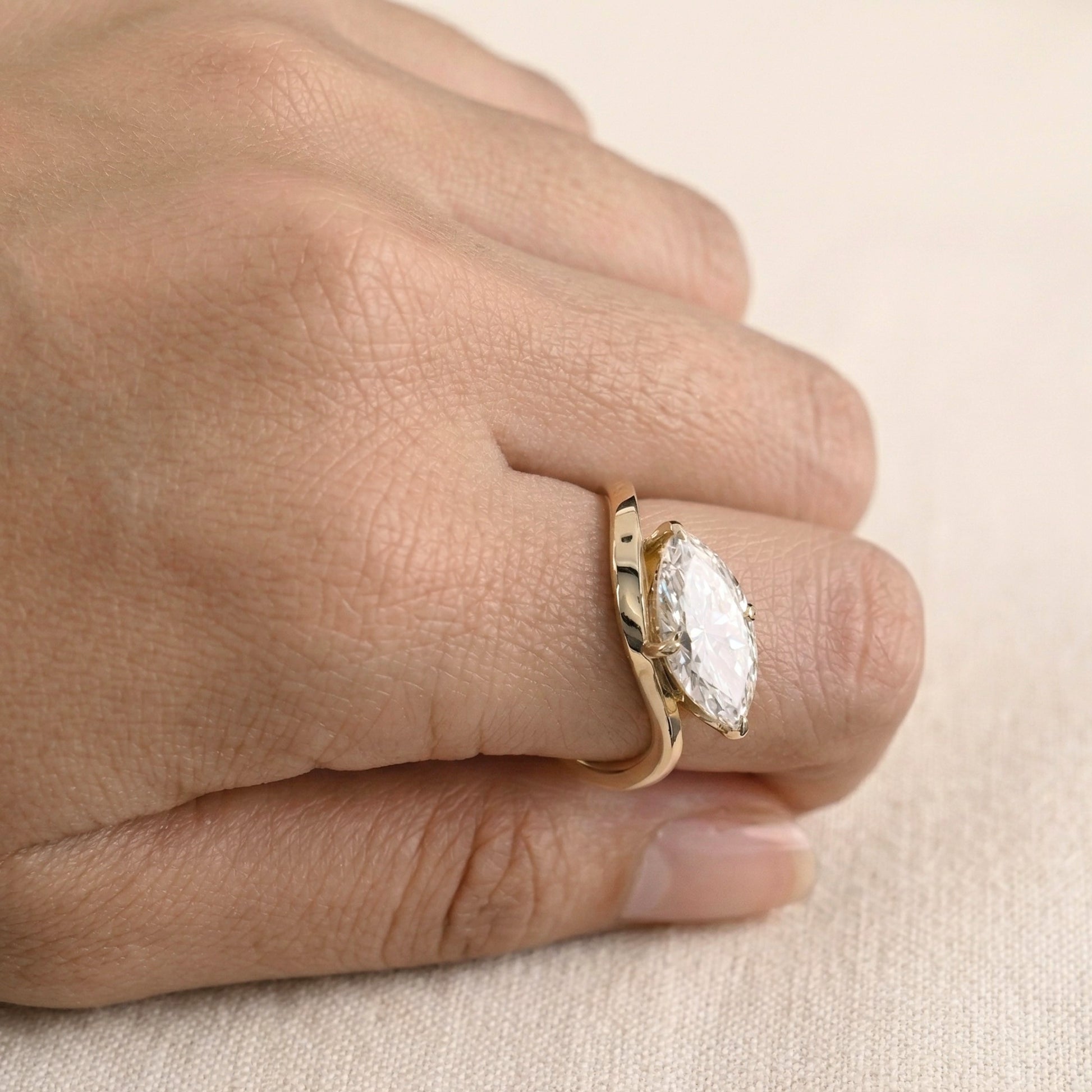 Gold ring with a large diamond on a hand against a beige background