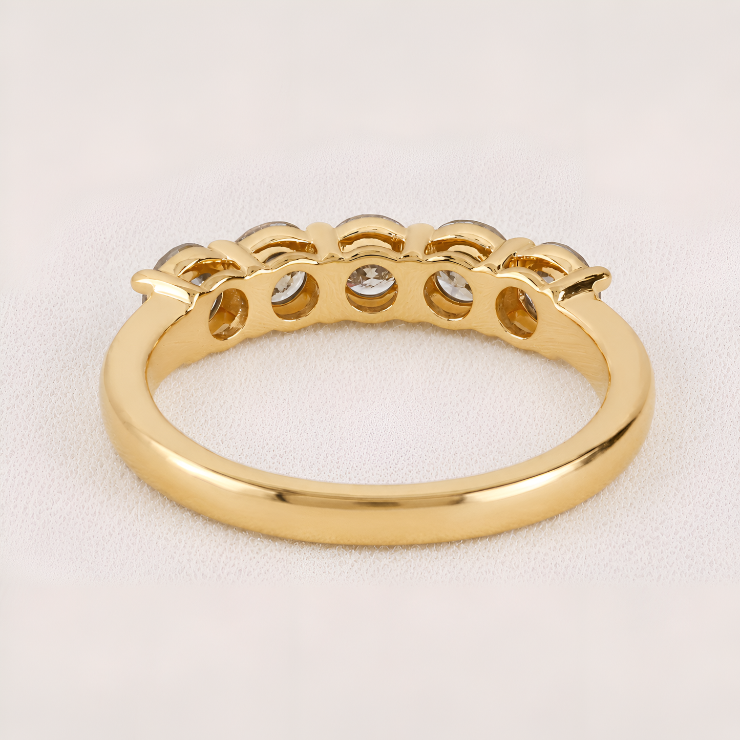 A yellow gold ring with a decorative scalloped top featuring five small clear gemstones, shown on a light beige textured background.