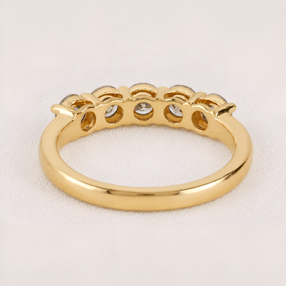 A yellow gold ring with a decorative scalloped top featuring five small clear gemstones, shown on a light beige textured background.