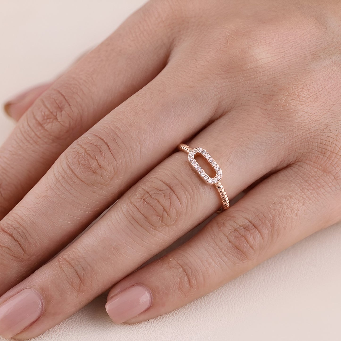 Rose gold ring with diamonds on a hand against a beige background