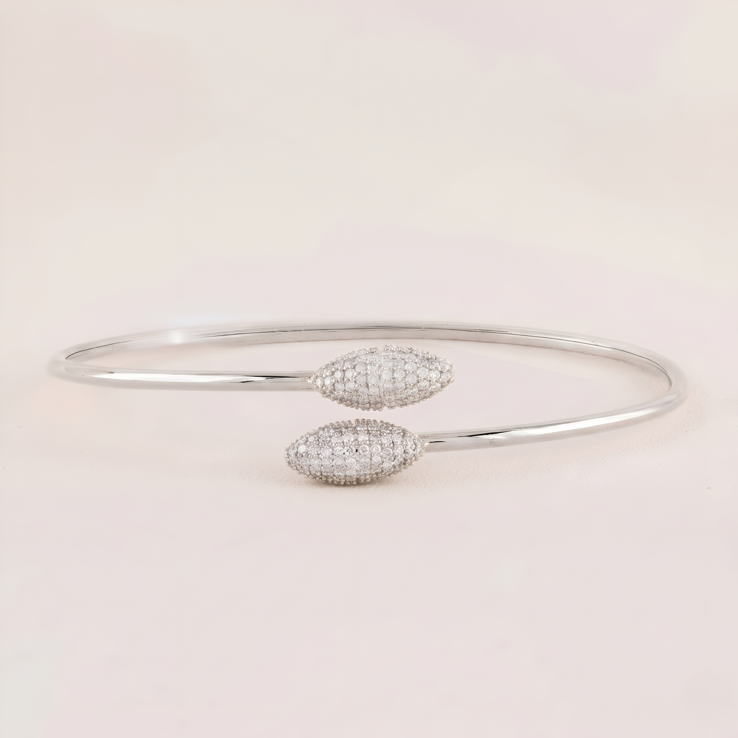 Silver bangle with two diamond-like stone pendants on a light pink background