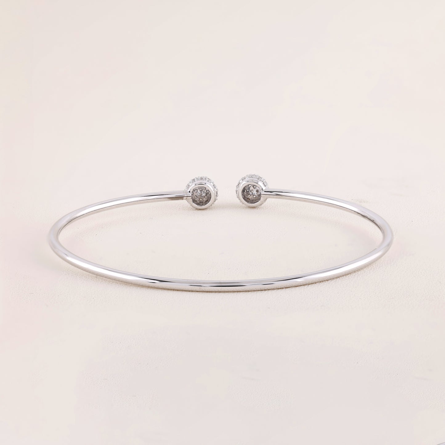 Silver bracelet with two round silver charms on a light pink background