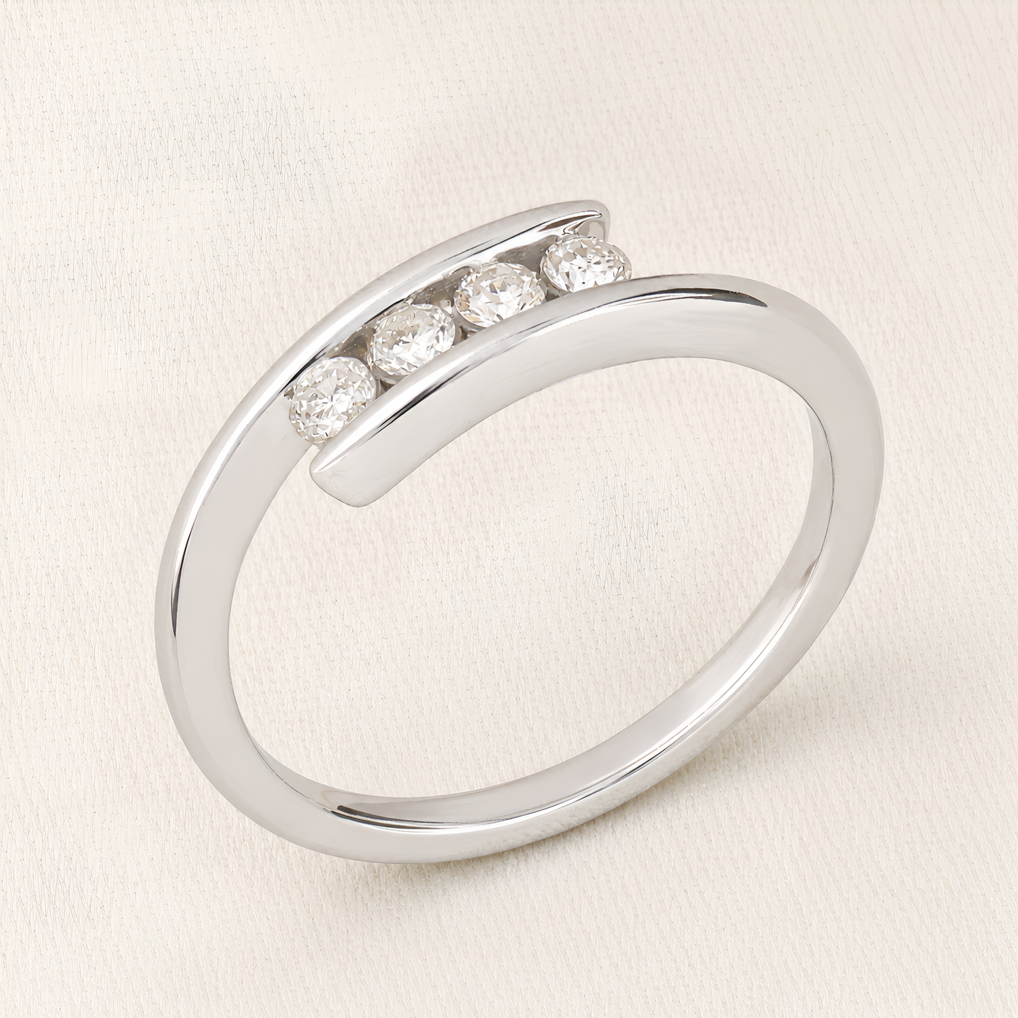 A polished silver-toned open band ring featuring four round-cut clear gemstones set in a curved row, photographed on a light cream fabric background.