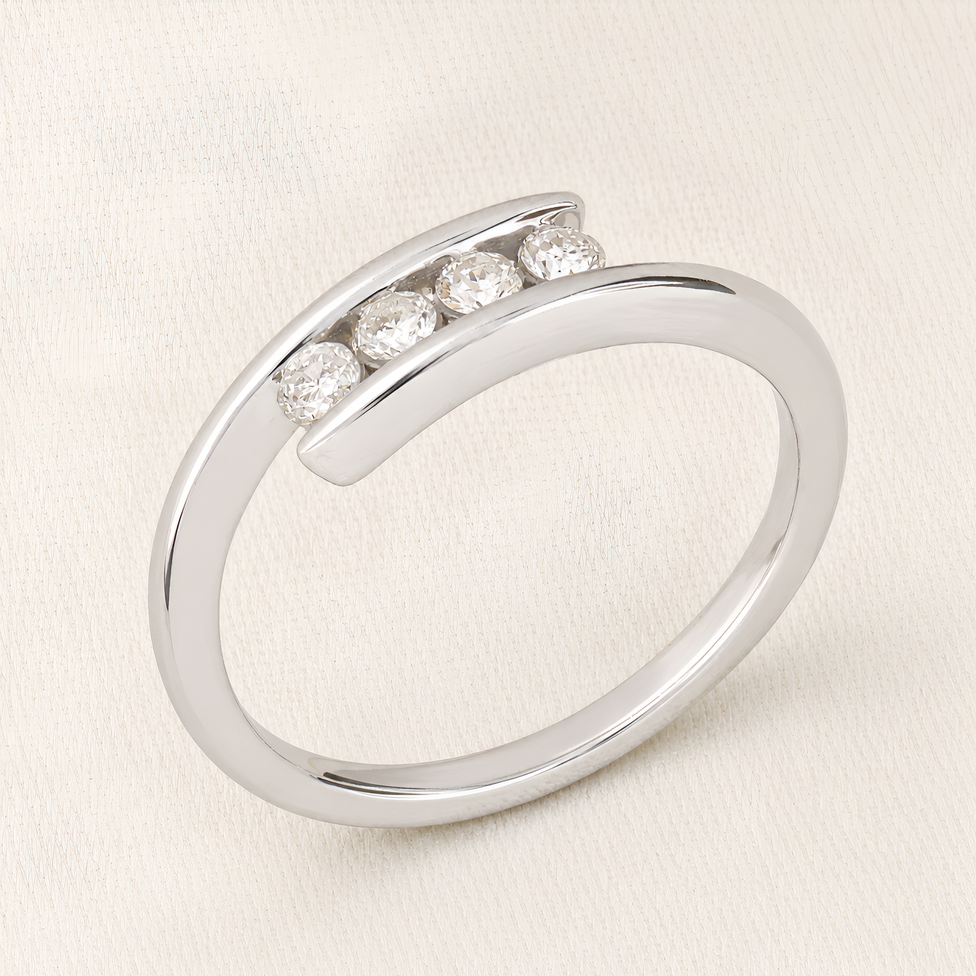 A polished silver-toned open band ring featuring four round-cut clear gemstones set in a curved row, photographed on a light cream fabric background.