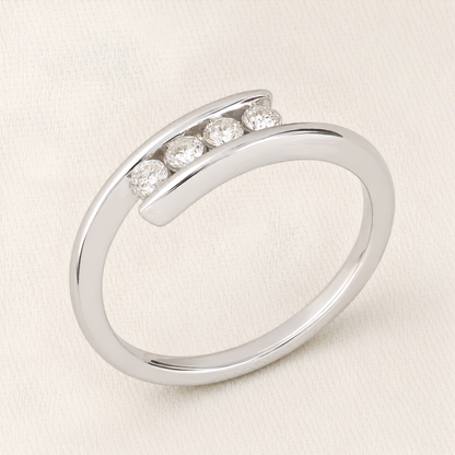 A polished silver-toned open band ring featuring four round-cut clear gemstones set in a curved row, photographed on a light cream fabric background.