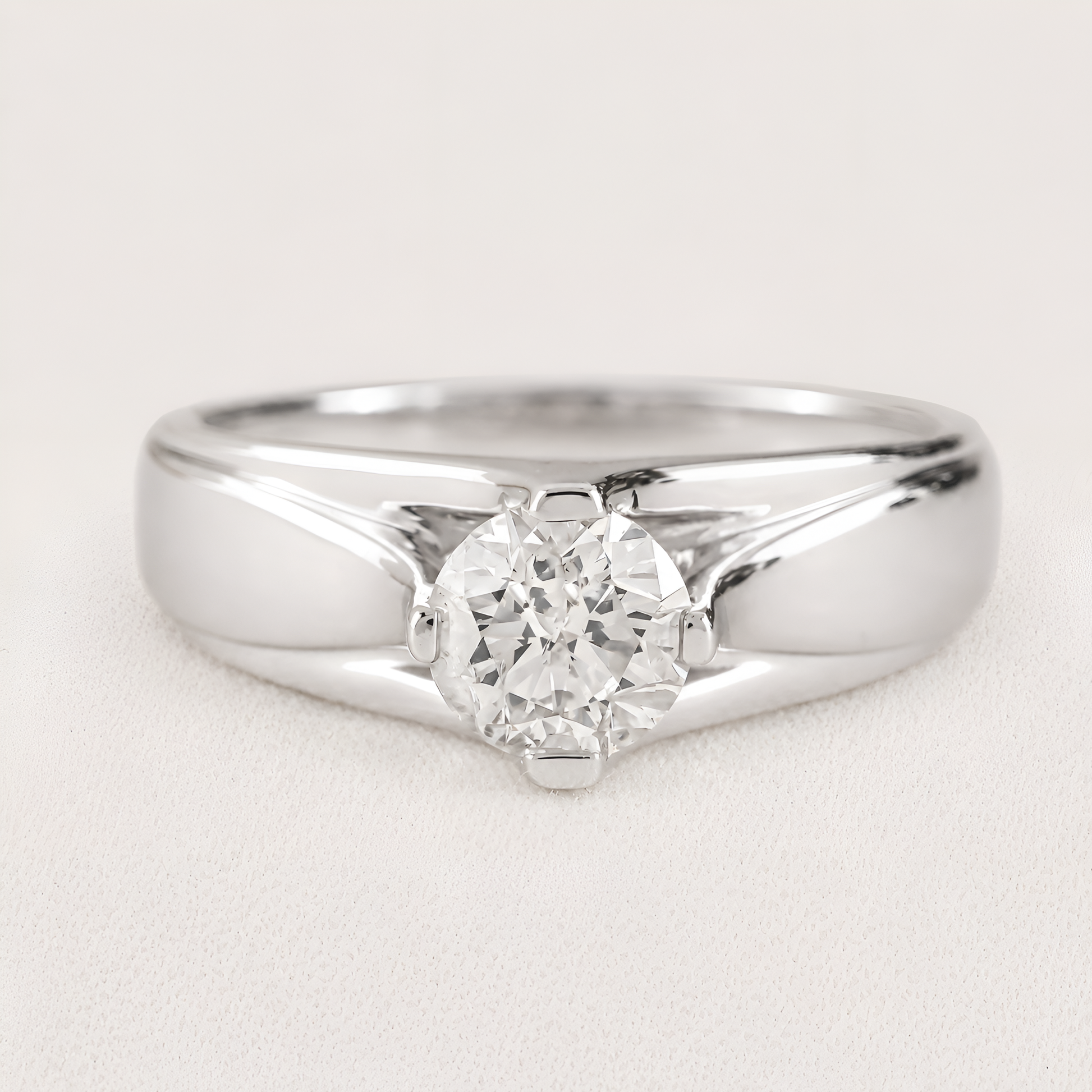 A classic solitaire engagement ring featuring a round brilliant-cut diamond set in a polished silver-colored metal band, shown on a light textured background.