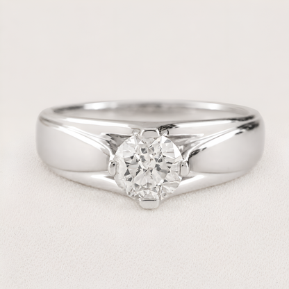 A classic solitaire engagement ring featuring a round brilliant-cut diamond set in a polished silver-colored metal band, shown on a light textured background.