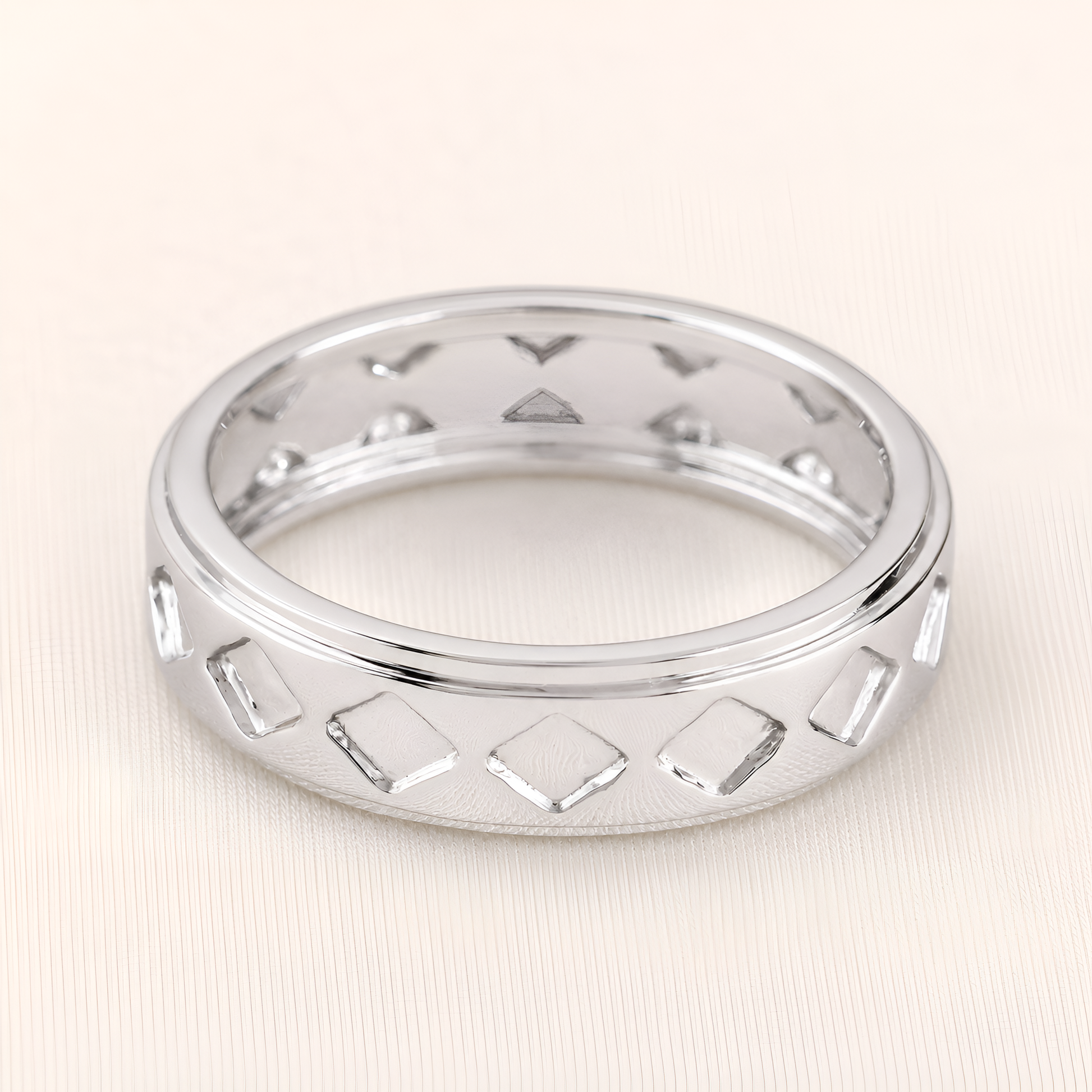 A silver band ring featuring a repeating pattern of open diamond-shaped cutouts, shown on a light beige textured background.