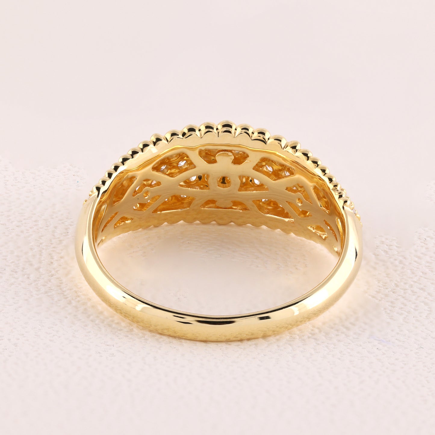 Gold ring with intricate design on a light pink background