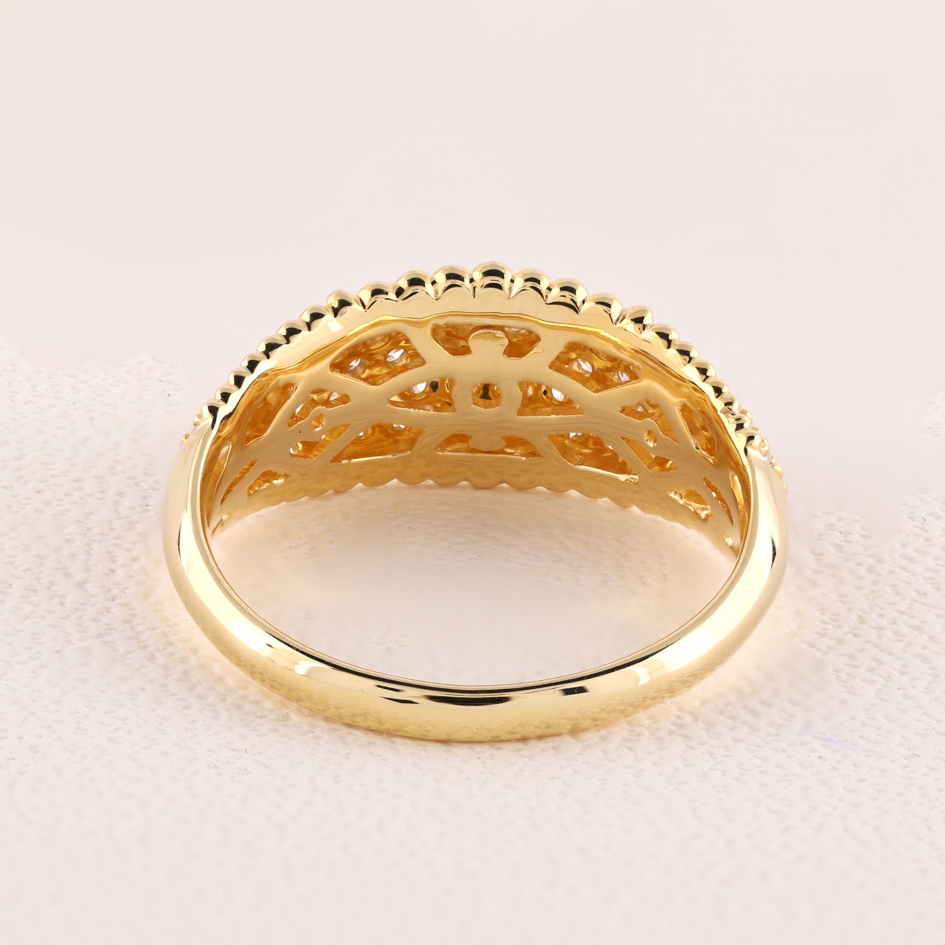 Gold ring with intricate design on a light pink background