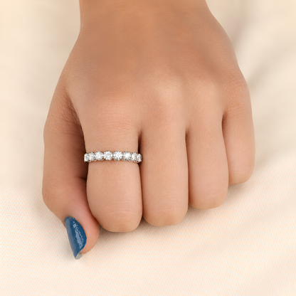 A close-up of a hand wearing a thin silver eternity ring set with small clear stones, resting on a soft beige fabric background.