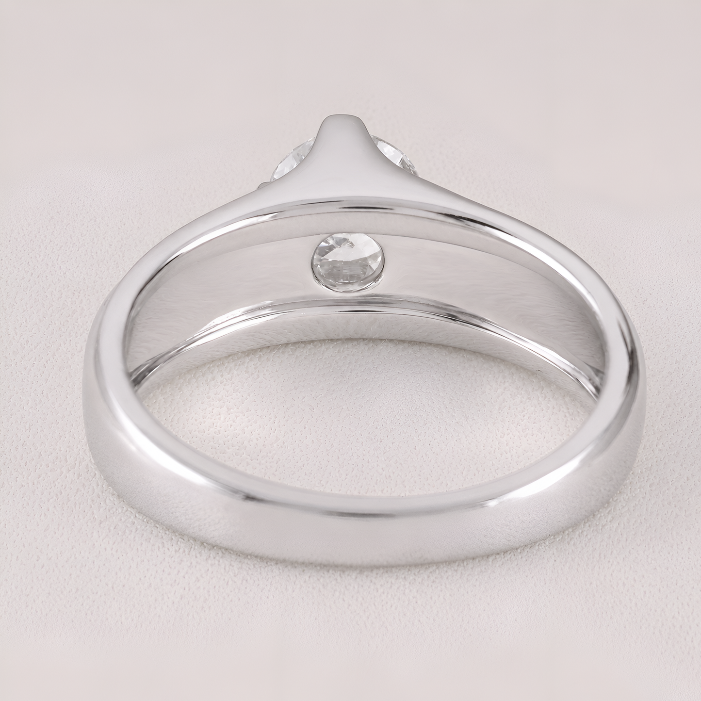 A silver-toned ring with a smooth polished band and a single round clear gemstone, shown on a light neutral background.