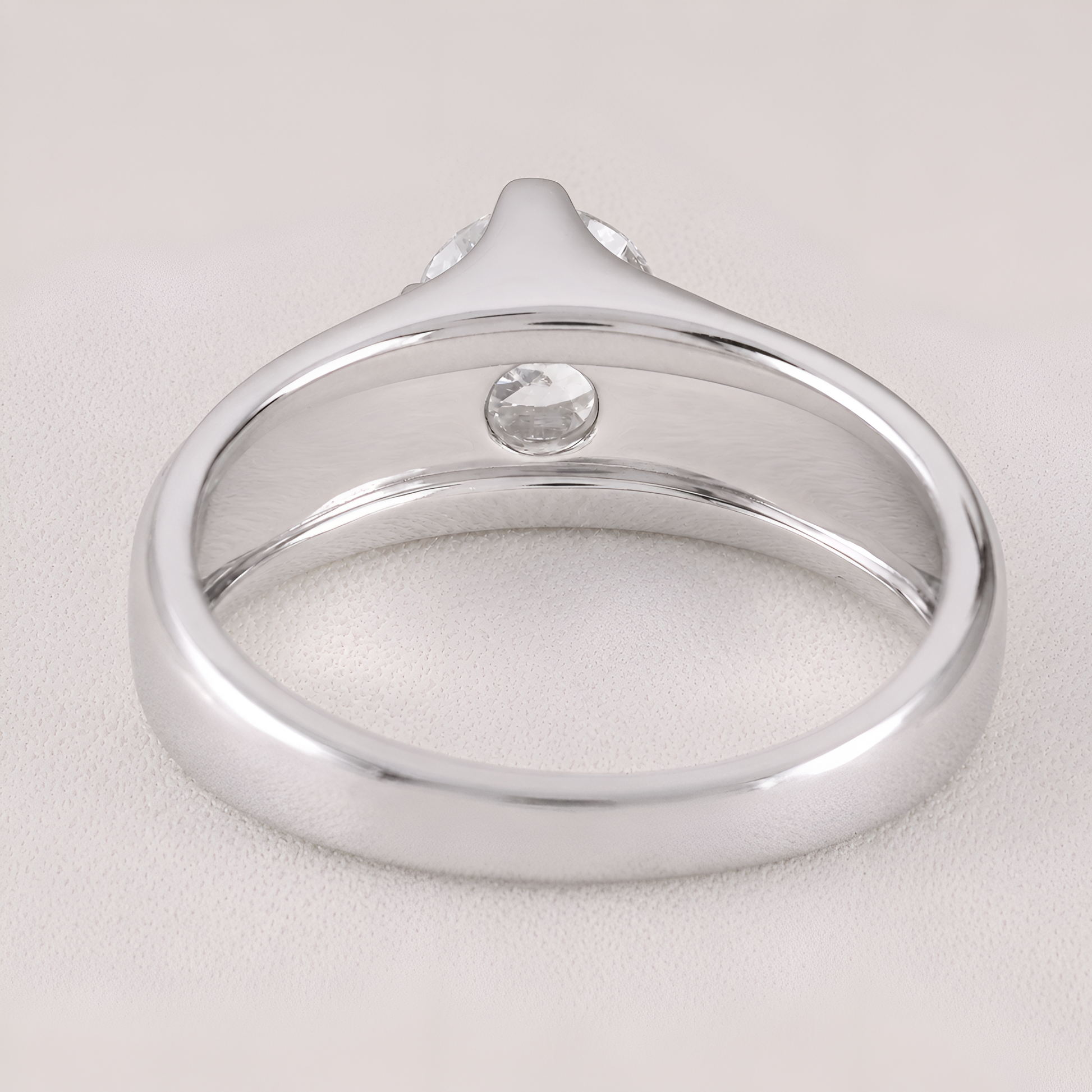 A silver-toned ring with a smooth polished band and a single round clear gemstone, shown on a light neutral background.