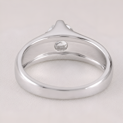 A silver-toned ring with a smooth polished band and a single round clear gemstone, shown on a light neutral background.